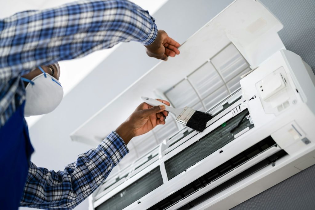 Man uses a small brush to clean the indoor air conditioning unit